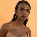 A person wearing gold-plated brass earrings with white cubic zirconia and black onyx, featuring a geometric design.