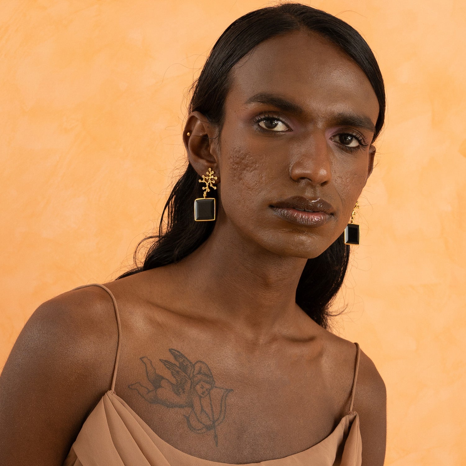 A person wearing gold-plated brass earrings with white cubic zirconia and black onyx, featuring a geometric design.