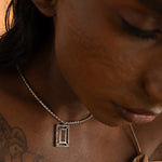 A person with a tattooed arm wearing a VAZIO PENDANT necklace with a white cubic zirconia pendant.