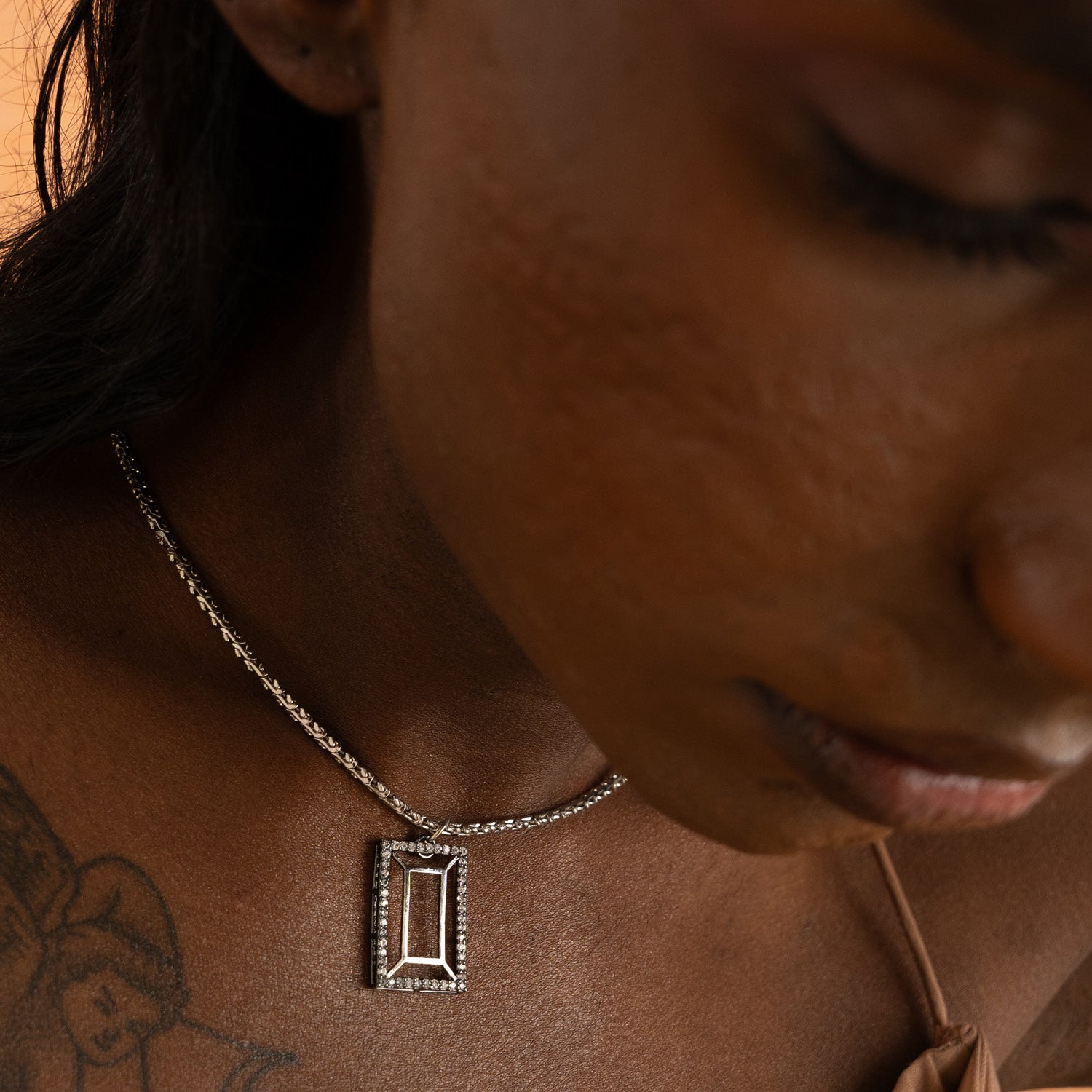 A person with a tattooed arm wearing a VAZIO PENDANT necklace with a white cubic zirconia pendant.