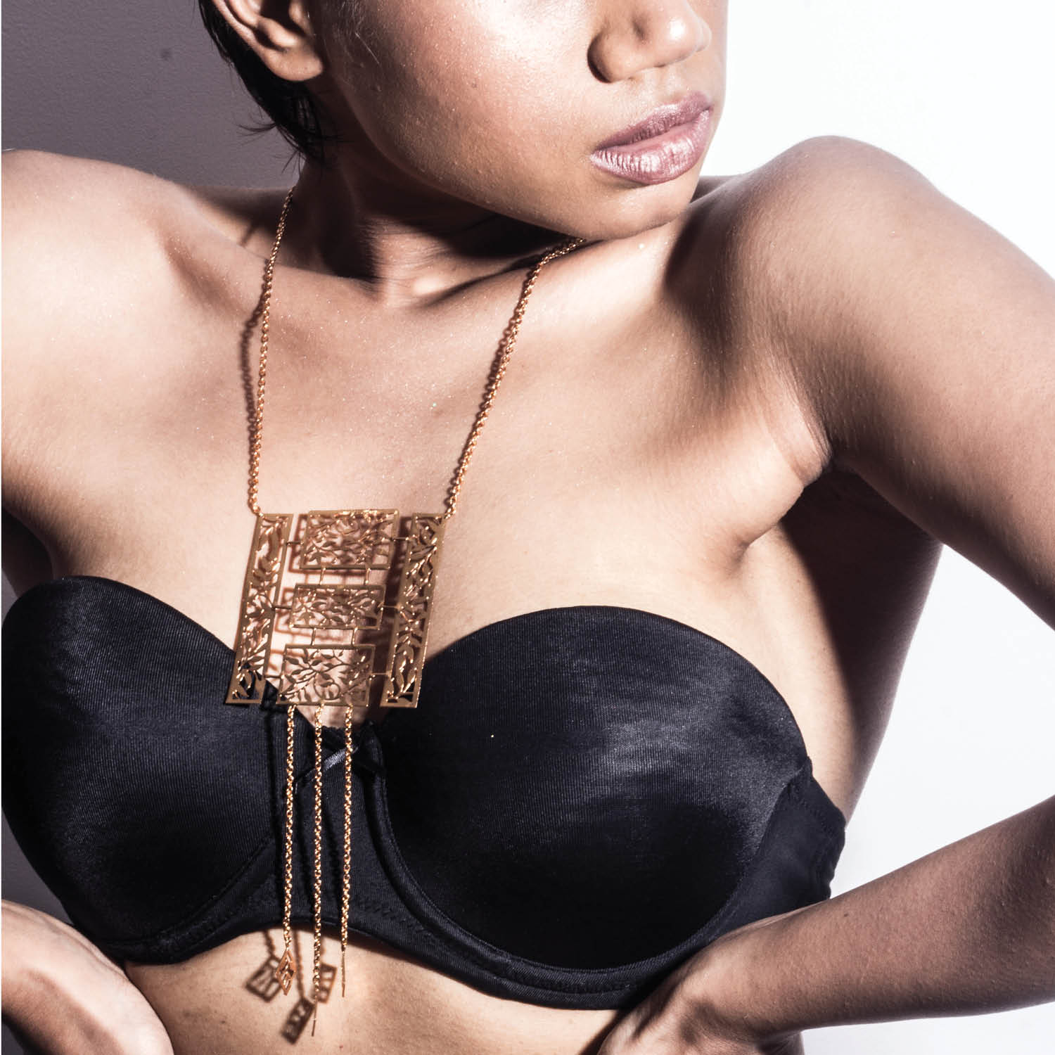 A person wearing a black top showcasing a gold-colored brass pendant necklace with intricate designs.