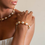 A person wearing a gold-colored bracelet with white baroque pearls.