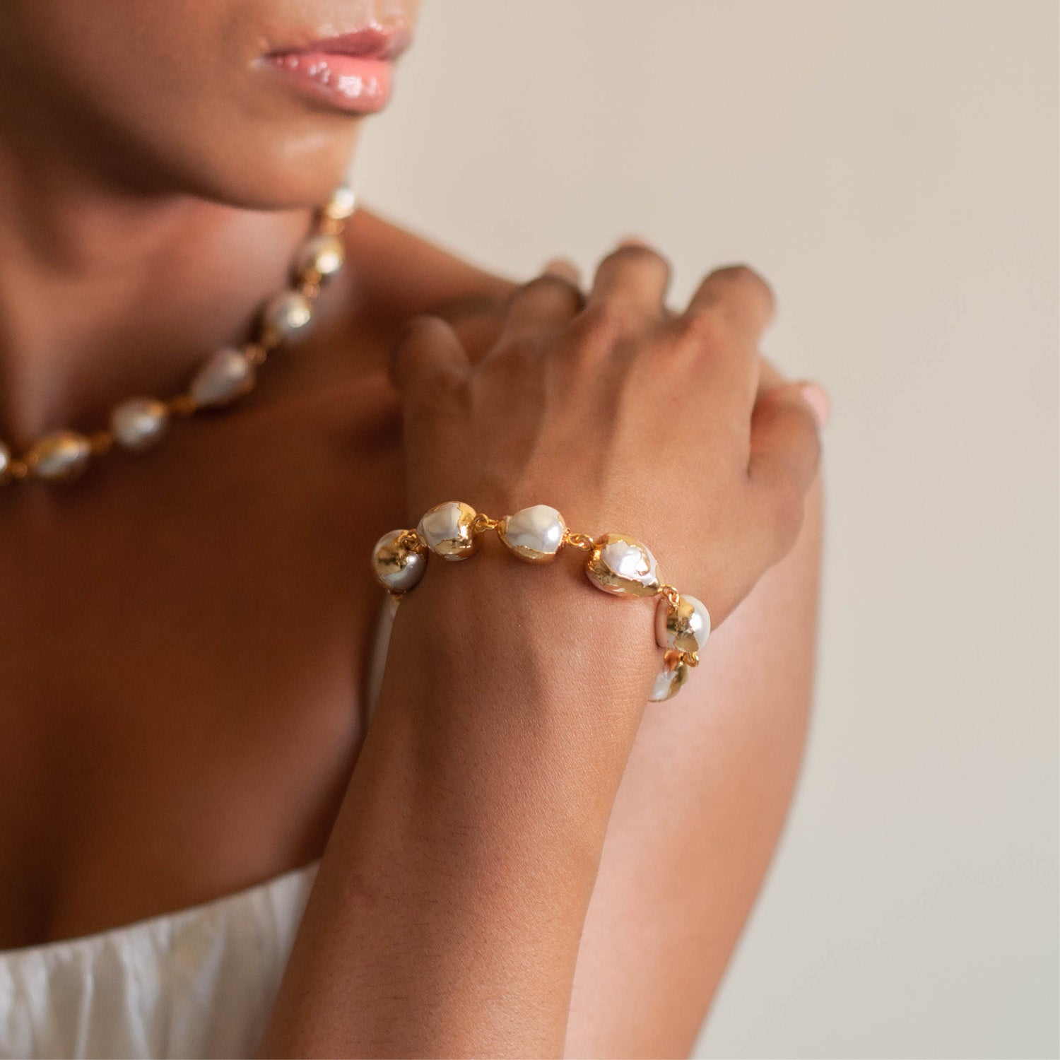 A person wearing a gold-colored bracelet with white baroque pearls.