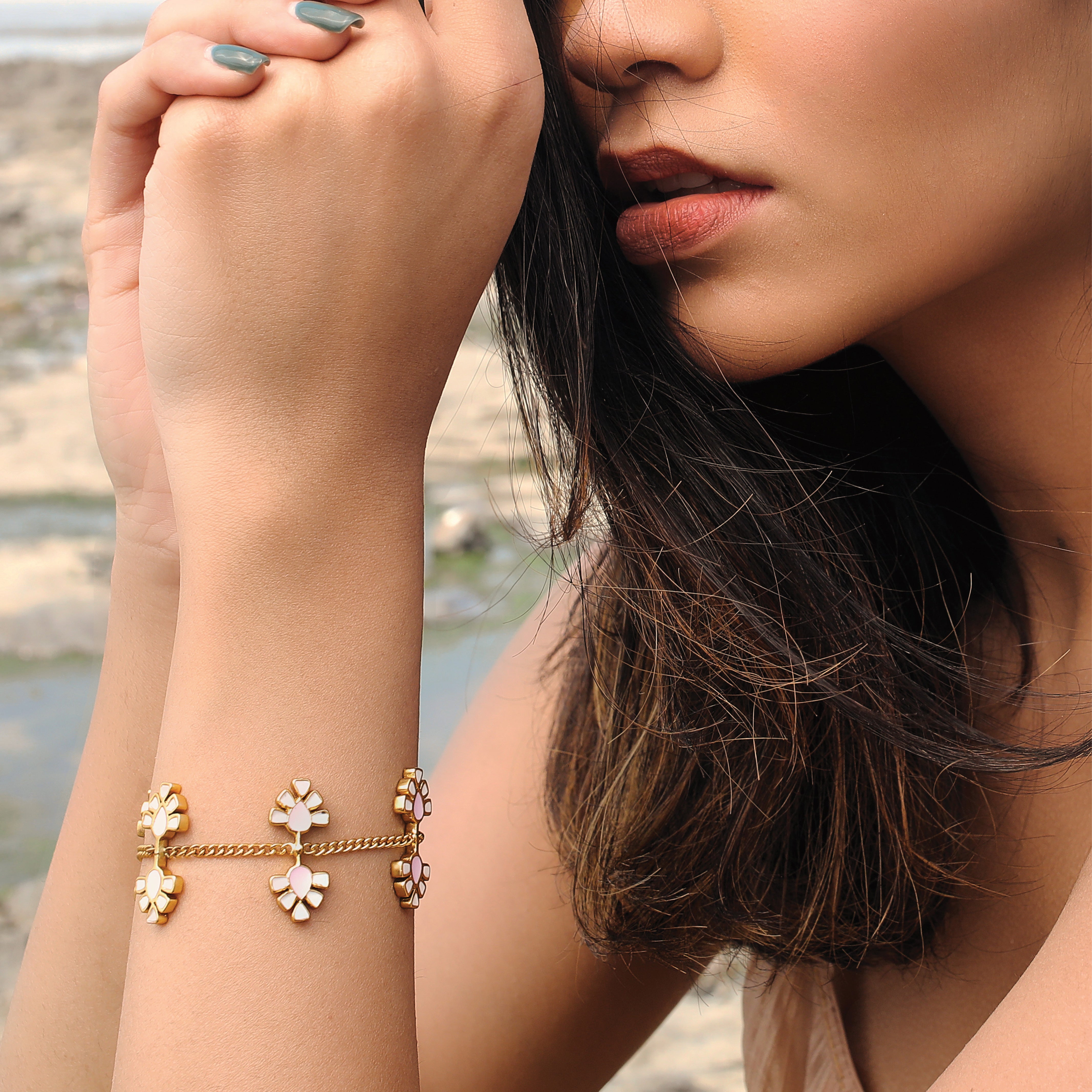 A person wearing a gold-plated bracelet with blush pink and white enamel details on their wrist.